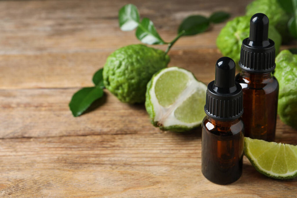 Bottles of essential oil and fresh bergamot fruits on wooden table. Space for text - Photo, image