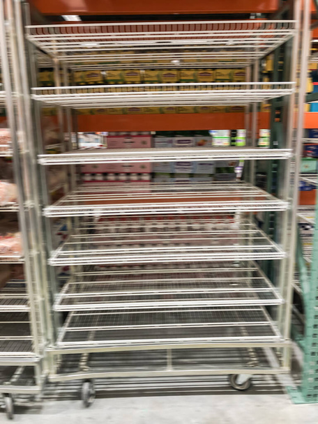 Blurry empty shelves at wholesale store near Dallas, Texas, America. Supermarket with empty steel shelving with wheels casters because of food shortage and supply chain crisis - Photo, Image