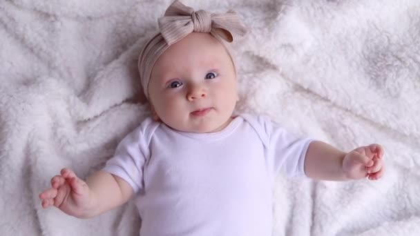 Κάτοψη πορτρέτο ενός χαριτωμένου νεογέννητου μωρού τριών μηνών ξαπλωμένο στην πλάτη του σε μια λευκή κουβέρτα και κοιτάζοντας την κάμερα. Η έννοια της παιδικής ηλικίας, της νέας ζωής, της μητρότητας. - Πλάνα, βίντεο