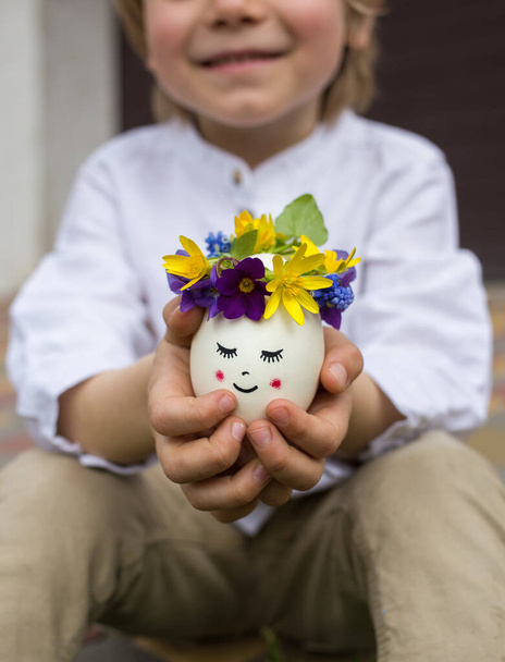 дитячі руки тримають миле пасхальне яйце з намальованим обличчям. Позитивне мислення, творчі ідеї. Зі святом Великодня. вибірковий фокус. Великодня концепція, веселе дитинство
 - Фото, зображення