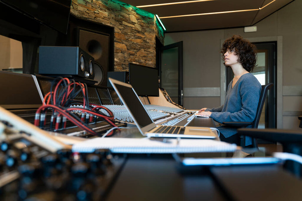 Genç kıvırcık saçlı beyaz kadın müzik stüdyosunda çalışıyor. - Fotoğraf, Görsel