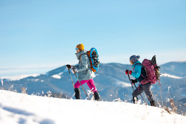 Twee vrouwen wandelen door de sneeuw tijdens een winterwandeling, twee in de bergen in de winter, wandeluitrusting, sneeuwschoen - Foto, afbeelding