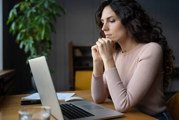 Przemyślane spojrzenie kobiety na monitor laptopa poważnie rozwijać strategię biznesową lub plan projektu rozważanie - Zdjęcie, obraz