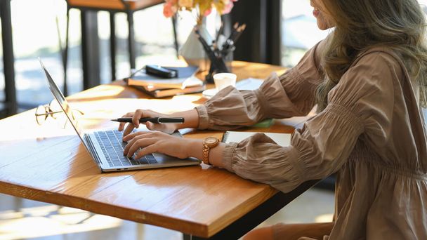 Widok z boku, Elegancka pracownica pracująca na laptopie notebooka w kawiarni co-working space. - Zdjęcie, obraz