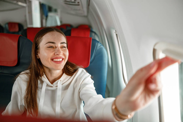 Fröhliche junge Frau schaut im Flugzeug aus dem Fenster - Foto, Bild