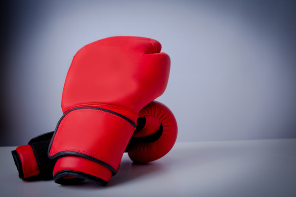 Rode bokshandschoenen over grijze achtergrond. Het overwinnen van uitdagingen als een groep van blauwe bokshandschoenen die samenkomen op een enkele rode handschoen als een zakelijk symbool van een moeilijke concurrerende omgeving. - Foto, afbeelding