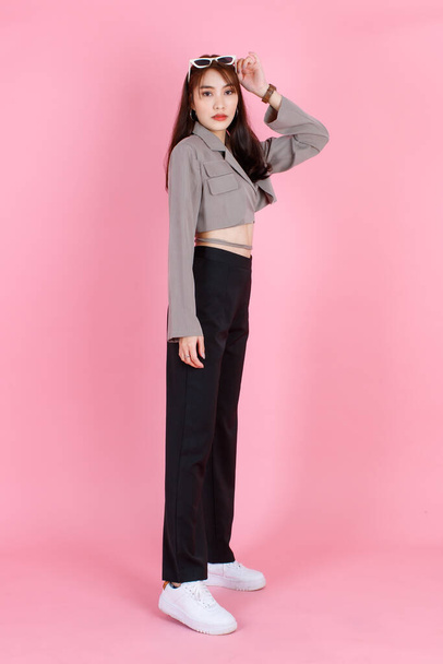 Portrait-Studioaufnahme von asiatischen jungen urbanen trendigen weiblichen Hipster Teenager-Mode-Model in lässigen Crop Top Street trägt Jacke mit Sonnenbrille auf dem Kopf stehen Blick in die Kamera auf rosa Hintergrund. - Foto, Bild