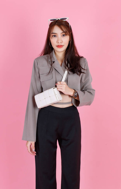 Portrait-Studioaufnahme von asiatischen trendigen weiblichen Hipster-Teenager-Modell in lässigen Crop Top Street trägt Jacke Sonnenbrille trägt Lederhandtasche Handtasche Handtasche im Stehen Blick in die Kamera auf rosa Hintergrund. - Foto, Bild