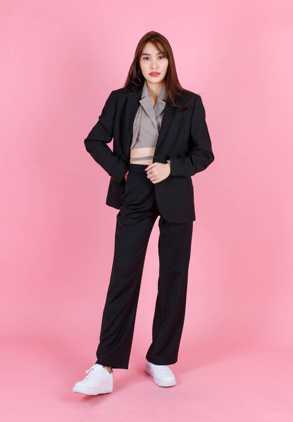 Portrait Studioaufnahme von asiatischen schönen städtischen trendigen modernen langen Haaren weibliche Hipster Teenager-Modell in lässigem schwarzen Anzug mit bauchfreiem Hemd im Stehen Blick in die Kamera auf rosa Hintergrund. - Foto, Bild