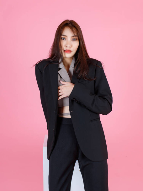 Portrait studio shot of Asian beautiful urban trendy modern fashionable long hair female hipster teenager model in casual black suit with crop top shirt standing look at camera on pink background. - Foto, imagen