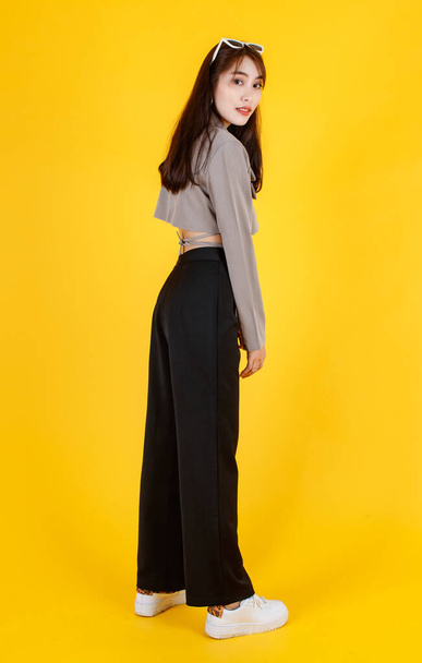 Portrait studio full body shot of Asian urban trendy modern fashionable long hair female hipster teen model in casual street wears crop top shirt standing posing look at camera on yellow background. - Photo, Image