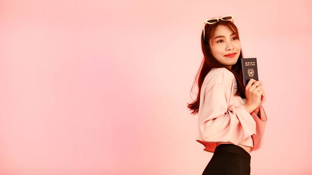 Portrait studio shot of Asian Korean female hipster teenager traveler in casual street wears and sunglasses standing look at camera holding showing blue republic of Korea passport on pink background. - 写真・画像