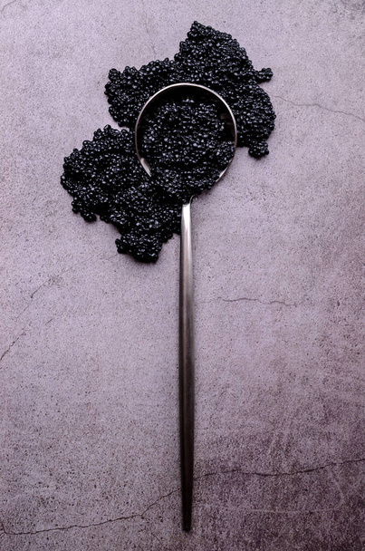Caviar noir salé dans une cuillère en métal sur un fond de pierre sombre. Espace de copie. Vue du dessus. - Photo, image