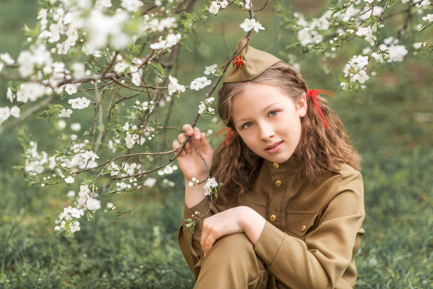 Portrét dívky ve vojenské uniformě na Den vítězství 9. května v kvetoucí zahradě - Fotografie, Obrázek