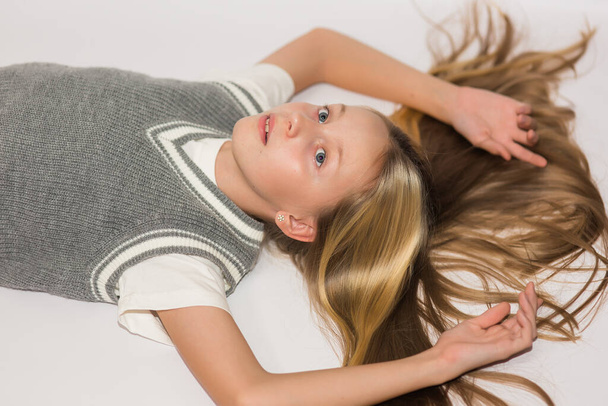 Portrait of a pensive beautiful teenager girl with long hair and blue eyes, looking at the camera, lying on the floor on a white background - Foto, Imagen