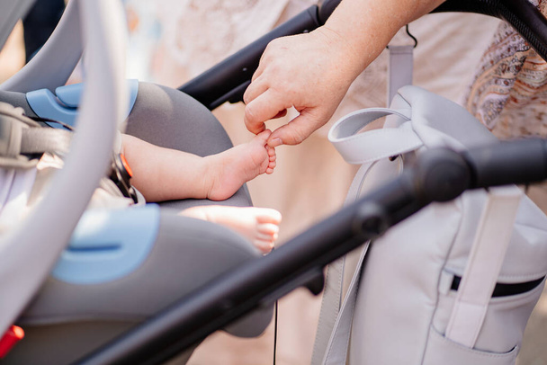 a womans hand touches a leg of a little boy sleeps strapped in a stroller. - Fotografie, Obrázek