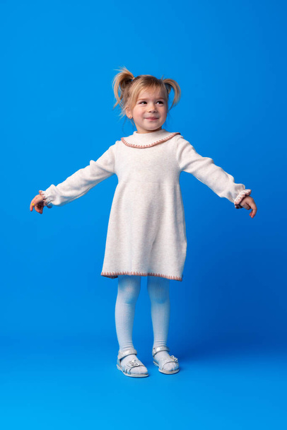 Full length portrait of a little girl standing on blue backgorund - 写真・画像