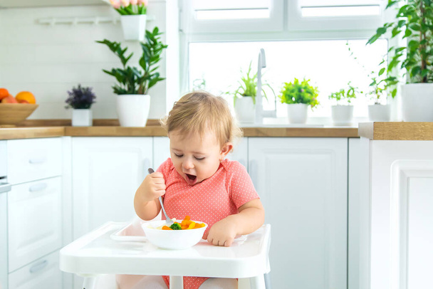 Vauva syö vihanneksia tuolilla. Valikoiva painopiste. - Valokuva, kuva