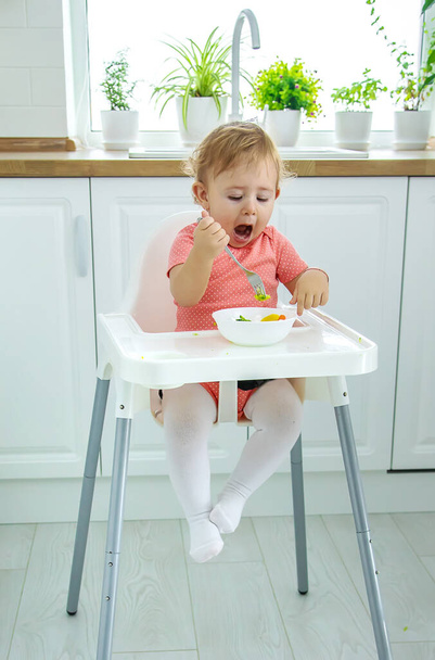The baby eats vegetables on a chair. Selective focus. - Φωτογραφία, εικόνα