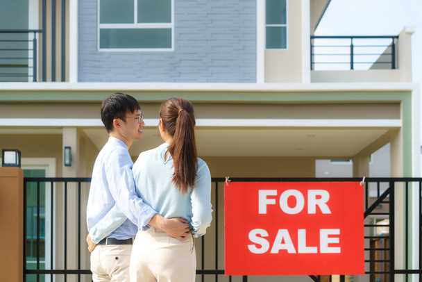 Back portrait of Asian young couple standing and hugging together looking happy in front of their new house to start new life. Family, age, home, real estate and people concept - Photo, Image