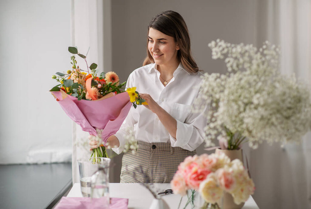 happy woman arranging flowers in vase at home - Zdjęcie, obraz