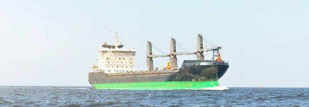 Μεγάλο πλοίο μεταφοράς χύδην φορτίου (φορτηγό πλοίο-γερανός) που πλέει στη Βαλτική Θάλασσα προς το λιμάνι της Ρίγας, Λετονία. Θέα από το γιοτ. Διεθνείς επικοινωνίες, εφοδιαστική, βιομηχανία, εμπορευματικές μεταφορές - Φωτογραφία, εικόνα