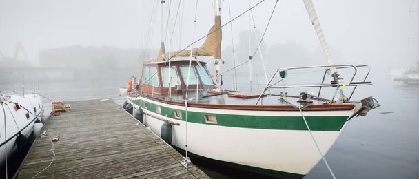Парусные лодки пришвартованы к пирсу в густом белом утреннем тумане на рассвете, крупным планом. Яхт клуб в Киле, Германия. Спорт, отдых, транспорт - Фото, изображение