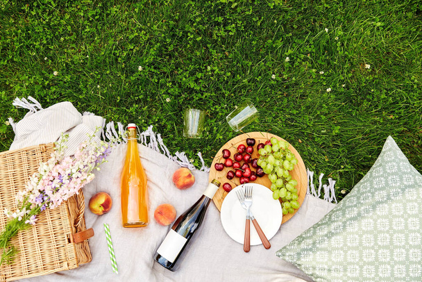 food, drinks and basket on picnic blanket on grass - Valokuva, kuva