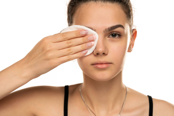 belle adolescente nettoie son visage avec des tampons de coton sur fond blanc - Photo, image