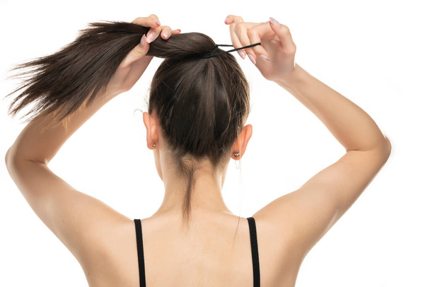 Rear view of a young woman tying her long hair on white background - Foto, Imagem