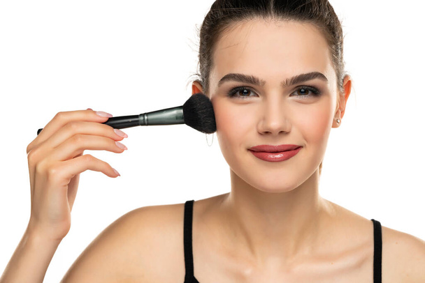 portrait of a smiling teen girl applying makeup with a makeup brush on her face on a white background - Photo, Image