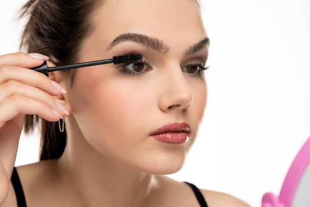 portrait of a teen girl applying mascara on her eyelashes on a white background - Photo, Image
