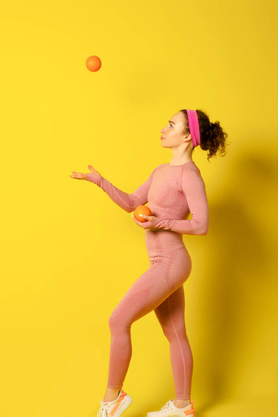 Athletic beautiful curly girl holding oranges on yellow background - Foto, Imagen
