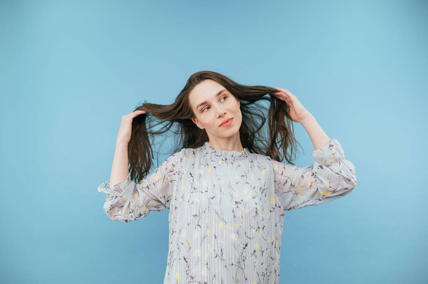 Attractive lady in a dress touches her hair on a blue background and looks away. - Foto, afbeelding