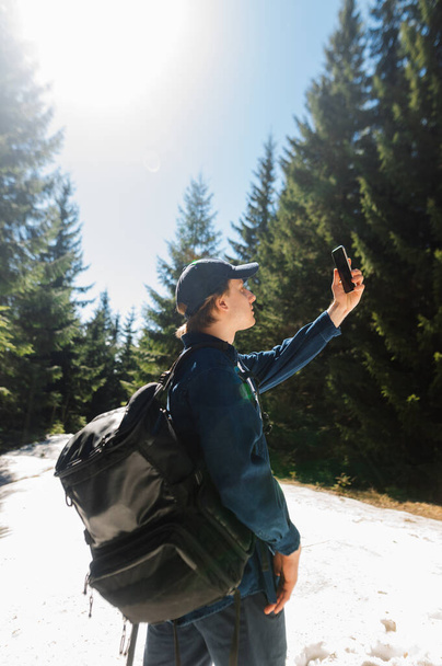 Caminante masculino en camisa y ropa casual en la cima de la montaña nevada captura la red en el teléfono inteligente con la mano levantada. Vertical - Foto, Imagen