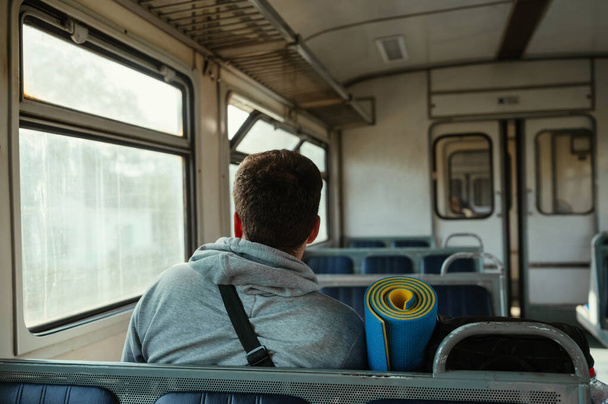 La schiena di un turista cavalca in un vecchio treno in montagna con zaino e tappetino sportivo. - Foto, immagini
