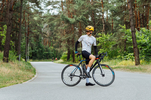 Atletisch mannelijk wielrenner in professionele outfit staat met een fiets op een bosweg. - Foto, afbeelding