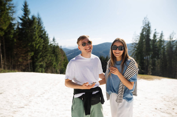 Happy man and woman hikers on a walk in the mountains in casual clothes standing in the snow on a background of mountain scenery and smiling looking at the camera. - 写真・画像
