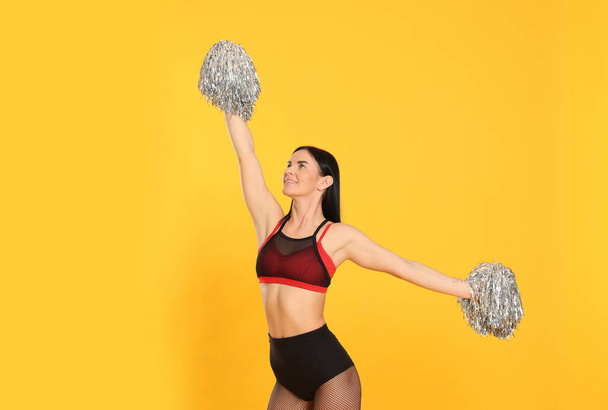 Beautiful cheerleader in costume holding pom poms on yellow background - Foto, Imagen