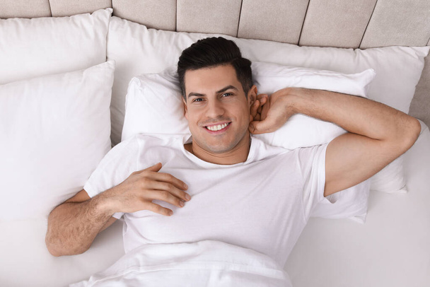 Happy man lying in bed at home, top view - Fotó, kép
