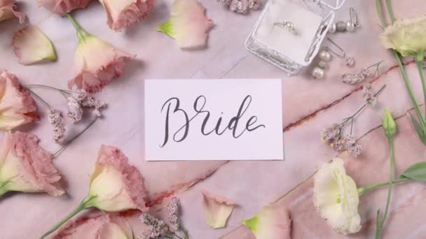 Tarjeta BRIDE en una mesa de mármol cerca de flores rosadas vista superior zoom  - Imágenes, Vídeo