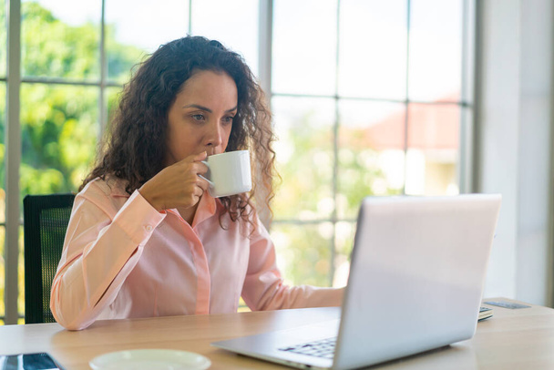 Donna latina che lavora con una tazza di caffè sullo spazio di lavoro a casa - Foto, immagini