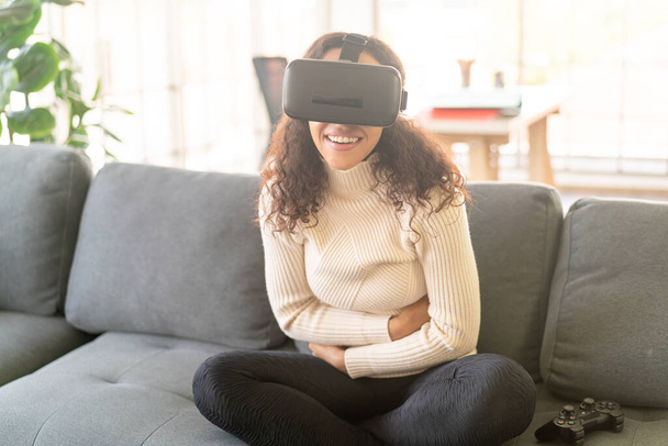 Latin woman using a virtual reality headset on sofa at home - Foto, afbeelding