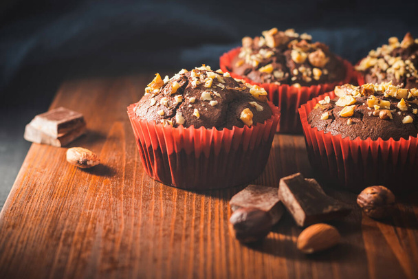 Domácí čokoládové muffiny nebo košíčky posypané ořechy na dřevěné desce. - Fotografie, Obrázek