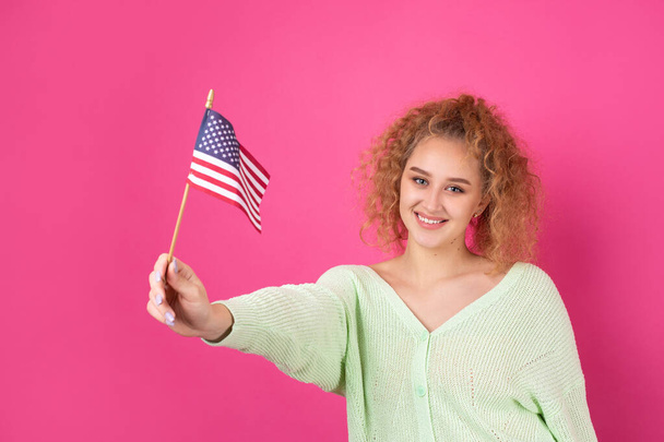 Yüzünde bir gülümseme olan genç mutlu bir kız ellerinde bir Amerikan bayrağı tutuyor. Vatanseverliğin ve özgürlüğün sembolü.. - Fotoğraf, Görsel