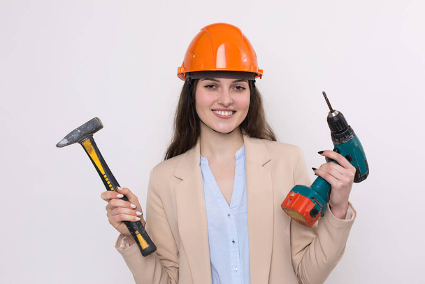Girl engineer in an orange construction helmet with a screwdriver and a hammer on a white background. - Photo, Image