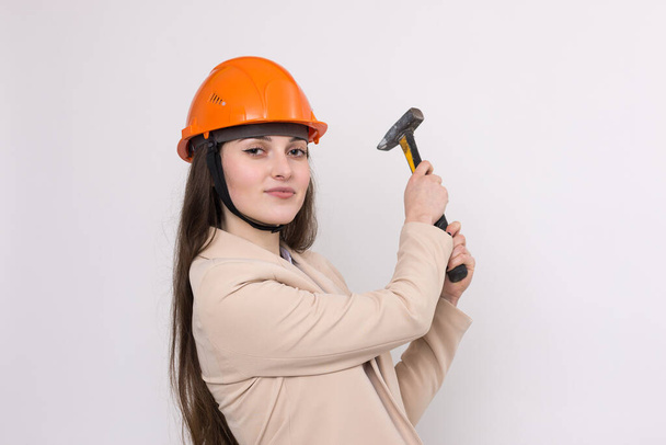 Dívka inženýr v oranžové stavební přilbě s kladivem na bílém pozadí. - Fotografie, Obrázek