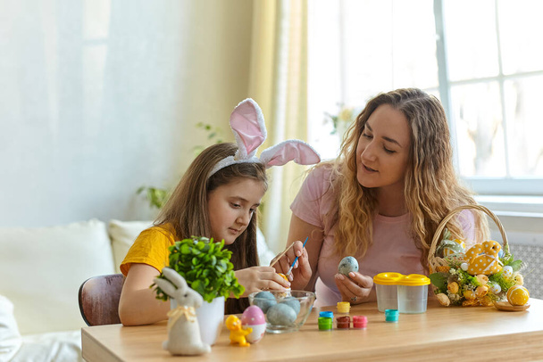 Mother and her daughter painting easter eggs. Happy family preparing for Easter. Cute little child girl wearing bunny ears. - Foto, afbeelding