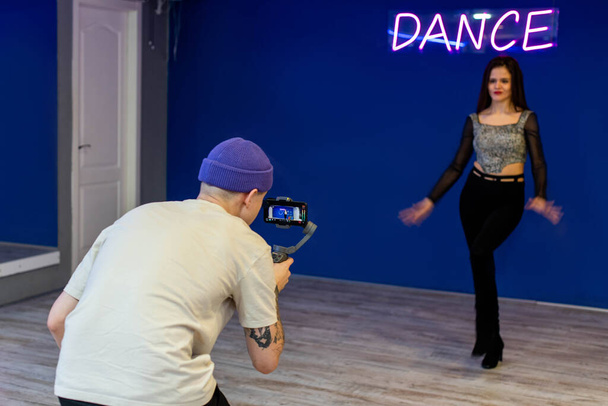 Blogger à la salle de gym tourne une vidéo avec une jeune danseuse entraîneuse sur un smartphone avec un stabilisateur de caméra manuel - Photo, image