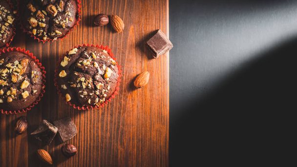 Homemade chocolate muffins or cupcakes sprinkled of nuts on a wooden board, top view. - Фото, зображення